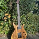 Elektrická kytara s přírodním dřevěným povrchem těla a hnedým krčkem. Nástroj má dva černý humbuckery, dvě kontrolní knoflíky a přepínač. Na hlavě kr…