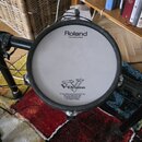 Fotografie zachycuje část elektronické bicí sady. Na bílém bubnovém povrchu jsou čitelné nápisy Roland, Head made by REMO a V-Drums spolu s doprovodn…