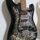 Elektrická kytara s černým bodies, které je zdobeno šedivým ornamentem v paisley stylu. Nástroj má hnědý hmatník a tři snímače typu single-coil. Na k…