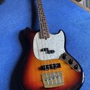 Elektrická basová kytara s tělem v provedení sunburst a bílým perleťovým pickguardem. Na hlavě hředu je viditelné logo Fender. Nástroj má dva snímače…
