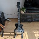 Elektrická kytara s tmavým, gradientním lakem v černé a šedé barvě. Na hlavě hрифu je bílý nápis Harley Benton a pod ním logo v podobě stylizovaného…