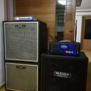 Sada basových zesilovačů a reproduktorů. Vlevo jsou dva stohované kabiny s mřížkou, které nesou logo GK a nápis NEO. Vpravo je černá kabina s nápisem…