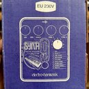 Modrá krabice s bílým nápisem EU 230V na nálepse. Na povrchu je bílý schéma efektového pedálu s nápisy DRY, VOL, SYNTH, CTRL 1 a CTRL 2. Uprostřed je…