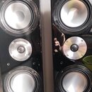 Dvě černé reproduktorové bedny s lesklým povrchem. Každá obsahuje dva stříbrné membránové reproduktory a jeden menší stříbrný vysokofrekvenční reprod…