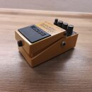 Zlatý kytarový efekt pedál značky BOSS s názvem Acoustic Simulator AC-3. Na horní straně jsou tři černé ovládací knoflíky a nápisy INPUT a AMP OUT. P…