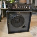Černý kytarový kombo zesilovač s reproduktorem za kovovou mřížkou a basreflexním otvorem. Horní ovládací panel obsahuje nápisy TUNE GAIN, BASS, MID a…