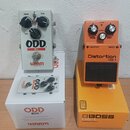 Dvě kytarové efektní pedály v krabicích. Vlevo je bílý pedal s nápisy ODD BOX v1 a WARM AUDIO, má tři černé oválové knoflíky označené Volume, Drive a…