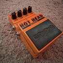 Oranžový kytarový efekt s černým povrchem v dolní části. Na šasi je uveden nápis HOT HEAD DISTORTION a logo DigiTech. Horní část obsahuje čtyři černé…