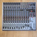 Stříbrný mixážní pult značky behringer s označením XENYX 2442USB. Zařízení obsahuje numerous vstupní konektory, posuvníky a ovládací knoflíky v modré…