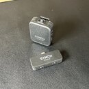 Dvě černé bezdrátové komponenty značky SYNCO. V horní části je transmitter s textem SYNCO Transmitter a v dolní části receiver s textem SYNCO Receive…