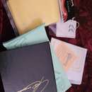 Sada příslušenství k hudebnímu nástroji na červeném podkladu. Je zde žlutý utírací hadřík v plastovém obalu s nápisem Gibson POLISH CLOTH, světle mod…