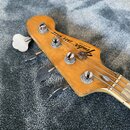 Hlava basové kytary z přírodního dřeva s nápisem Fender JAZZ BASS a sériovým číslem 5567275. Nástroj má čtyři kovové ladičky a viditelné opotřebení p…