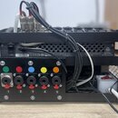 Černý rackový přístroj s pěticestným panelem, který obsahuje konektory XLR a jack. Nad konektory jsou umístěna barevné kontrolky v zelené, červené, m…