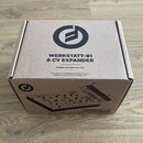 Kartonová krabice s černými nápisy a logem. Na horní straně je text WERKSTATT-01 & CV EXPANDER a pod ním Analög Synthesizer Kit spolu s informací o s…