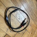 Černý audio kabel s rozdělením z jednoho konektoru na dva. Kabel má tři zlaté konektory typu jack. Jeden z konců je označen červým kroužkem u kabelu.