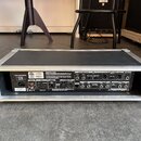 Zadní strana elektronického zařízení v hliníkovém transportním kufru s černým povrchem. Na panelu jsou viditelné různé konektory, přepínače a nápisy,…