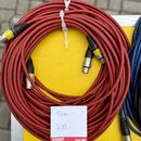 Červený kabel svázaný bílou plastovou stahovací spojkou. Kabel má na koncích konektory typu XLR, přičemž dva z nich mají žluté označení. Vedle kabelu…