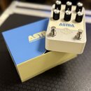 Kytarový efekt v bílém kovovém šasi s šesti černými kontrolními knoflíky. Na horní straně je modrý nápis ASTRA a pod ním text MODULATION MACHINE, dál…