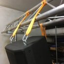 Černý reproduktor s mřížkou je zavěšen na hliníkovém truss systému pomocí tří oranžových textilních popruhů s kovovými háky. Na reproduktoru nejsou v…