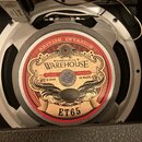 Fotografie zachycuje kytarový reproduktor s bílým rámem. Na středovém štítku je červenobílý nápis BRITISH INVASION a logo WAREHOUSE s doplňky ASSEMBL…
