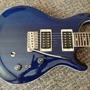 Modrá elektrická kytara s dvojstupňovými humbuckery a tremolo systémem. Na těle jsou dva ovládací knofíky a jeden přepínač. Povrch je v lesklém prove…