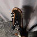 Fotografie zachycuje hlavu a hриф kytary z horní perspektivy. Nástroj má dřevěné provedení s viditnou masivní strukturou a černými ladičkami. Na dřev…