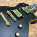 Černá elektrická kytara s matným povrchem a zlatým hardwarem. Na těle jsou dva humbuckery, kobylka a dva ovládací knoflíky v zlatém provedení. Na kyt…