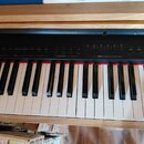 Černý digitální klavír s bílými a černými klávesami. Na ovládacím panelu jsou viditelné nápisy: LOWER VOICE, VOICE / MIDI CHANNEL, METRONOME / TOUCH…