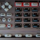 Detailní pohled na ovládací panel elektronického zařízení s nápisem COSM v horní části. Panel obsahuje řadu tlačítek, včetně červeně podsvícených pol…