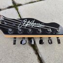 Černá hlava kytary s viditelným dřevěným základem a šesti ladicími kolíky. Na povrchu je bílý nápis CHAPMAN GUITARS a velký bílý podpis. Povrch je le…