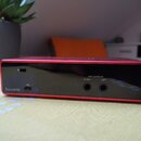 Zadní strana červeného audio rozhraní s černým zadním panelem. Jsou zde vidět dva výstupní konektory s nápisy LINE OUTPUTS, RIGHT a LEFT, USB port a…