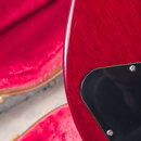 Detail korpusu elektrické kytary v červené barvě s viditelnou strukturou dřeva. Na korpusu je připevněn černý plastový pickguard s viditelnými šrouby…