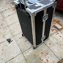 Černý transportní kufr (flightcase) s hliníkovými hranami a kovovými rohy. Je vybaven kolečky, dvěma horními úchyty a vysouvací rukojetí. Povrch vyka…