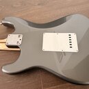 Zadní strana šedé elektrické kytary s kovovým krytem v oblasti krku a bílým plastovým krytem elektroniky. Na kovovém krytu je vyryto logo Fender a ná…