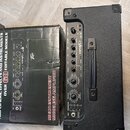 Černý kombo zesilovač s nápisem VXPX1 a logem Takamine, umístěný vedle své originální krabice. Zesilovač má ovládací prvky v horní části, včetně knof…