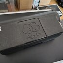 Černý plastový kufr s logem AKG vyraženým do víka. Na levé straně je nalepená bílá nálepka s ručně psaným nápisem 1500 Kč. Povrch kufrů vykazuje vidi…