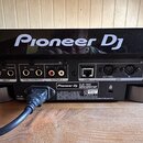 Zadní strana černého elektronického zařízení s nápisem Pioneer DJ. Jsou zde vidět různé konektory: RCA vstupy a výstupy, MIDI porty (OUT/THRU, IN), U…