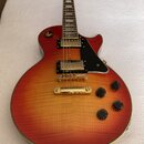 Elektrokytara s tělem v červeno-žlutém gradientu (sunburst) a viditelnou strukturou dřeva. Nástroj má zlatý hardware, dva humbuckery a černý pickguar…