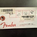 Bílá papírová štítková karta s červeným logem Fender. Karta obsahuje čárcové kódy a texty: C01600886, CLAPTON STRATOCASTER PTR a 0117602-843. U políč…