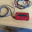 Červený USB zvukový interface s nápisy U-CONTROL, behringer a UCA222. Zařízení má na horní straně tři zlaté konektory a na přední straně porty USB, O…