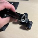 Černý cylindrický předmět s kovovým konektorem na konci, který drží ruka. Na povrchu je nápis MADE IN USA a symbol CE. Konec konektoru vykazuje známk…