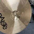 Zlatý kovový činel s koncentrickým žebrováním. Na povrchu je velký černý nápis PAiste a pod ním menší text MADE IN SWITZERLAND. V pravé části je vidě…