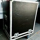 Černý transportní case s kovovými hranami a rohy. Povrch je viditelně opotřebovaný s mnoha škrábancemi a odřeninami. Case je vybaven dvěma madly na s…
