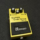 Žlutý kytarový efekt pedál s černým spodním panelem. Na horní části je nápis SUPER Over Drive SD-1w a logo BOSS, pod kterým je štítek s nápisem 技 WAZ…