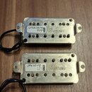 Dvě elektrické kytarové snímače s kovovým krytem stříbrné barvy. Horní snímač má nálepku s nápisem LPNA-V8-R2 BRIDGE 0905 RoHS a logo Ibanez. Dolní s…