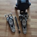 Sada bubnových pedálů značky TAMA s nápisem IRON COBRA 200 na šlapkách. Soubor obsahuje pravý a levý pedál, propojovací hřídel a černý plastový kufr.…