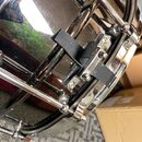 Detailní záběr na chromovaný obrubnice a napínací mechanismus bubnu. Na kovovém povrchu jsou viditelné drobné škrábance a nečistoty. K mechanismu je…