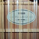 Detail vnitřní štítku akustické kytary s dřevěným povrchem. Na oválném světle štítku je uveden nápis YAMAHA a model FG-420-12. Dole je uveden text MA…