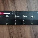 Černý efektový spínací systém s nápisem BOSS EFFECTS SWITCHING SYSTEM ES-8. Zařízení má digitální displej zobrazující červeně číslo 00.1 a osm kovový…