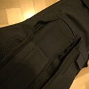 Detailní záběr na černý textilní obal na hudební nástroj. Na fotografii je vidět část popruku a švy v oblasti ramenní části. Povrch je vyroben z komb…